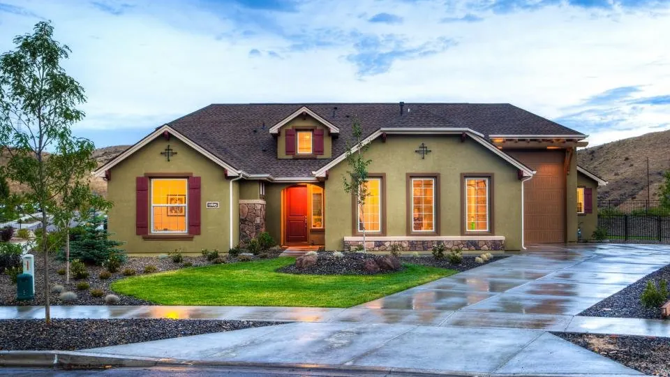A single-storey ranch-style house photographed after rain, with a low-pitched shingle roof and deep eaves