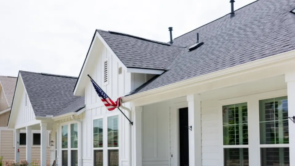 A white single-storey house with a grey shingle roof, front lawn and planted border