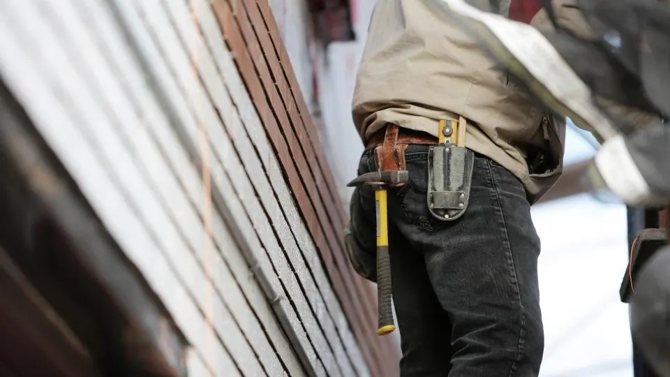 A tradesperson wearing a tool belt working alongside the edge of a roof